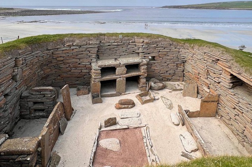 A stone structure with a circular layout, possibly a historical site, with a beach in the background. 1