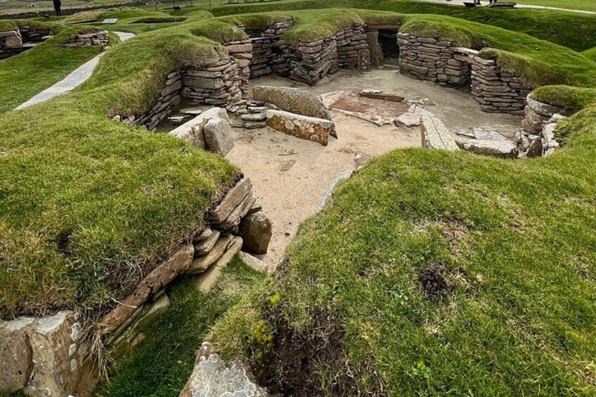 An archaeological site with stone structures and grassy mounds. 5