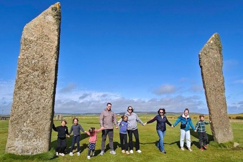 A group of people standing between two standing stones in a grassy field. 4