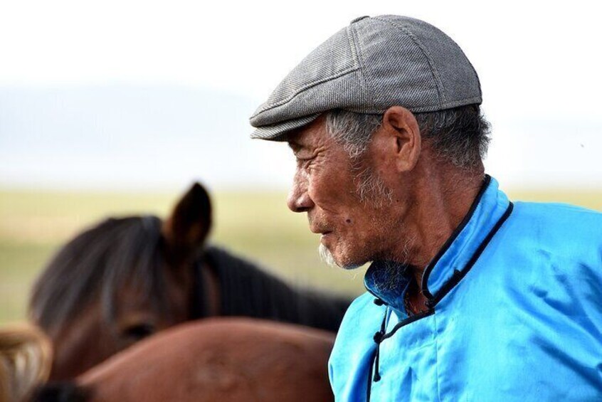A man in a blue shirt and cap with a horse in the background. 3