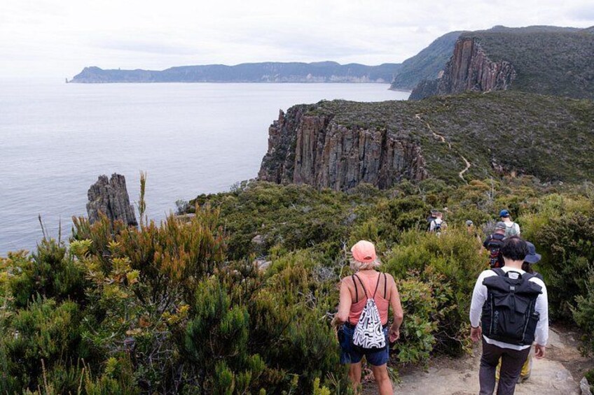 Hikers on a trail with a coastal view and rocky cliffs. 2
