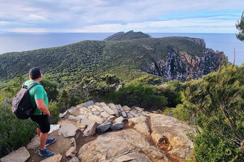 A hiker on a rocky path overlooking a coastal landscape with cliffs and greenery. 5
