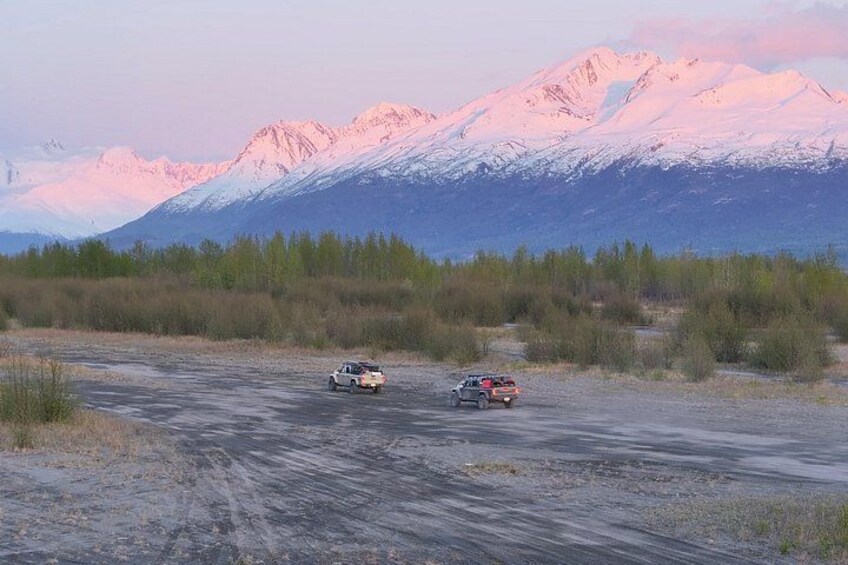 Two vehicles on a dirt road with snow-capped mountains in the background. 5