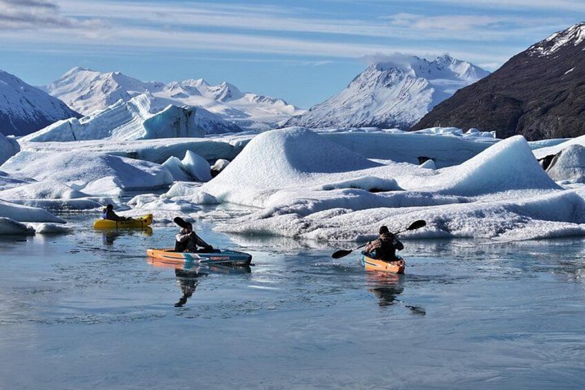 Kayakers on a frozen river surrounded by snow-covered mountains. 2