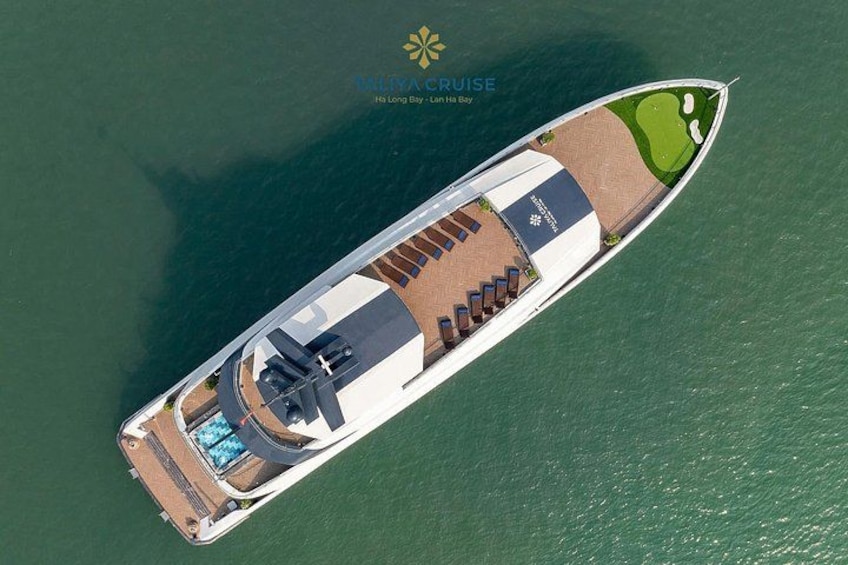 Eine Vogelperspektive auf ein Kreuzfahrtschiff mit Schwimmbecken, Liegestühlen und einer Grünanlage. 2