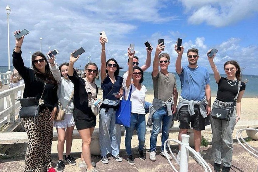 En gruppe mennesker på en bro, der bruger smartphones, med en klar himmel og havet i baggrunden. 1