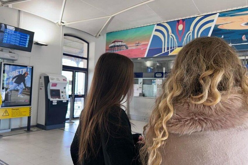 A ticketing area with a ticket machine, a digital display, and a colorful mural on the wall. 5