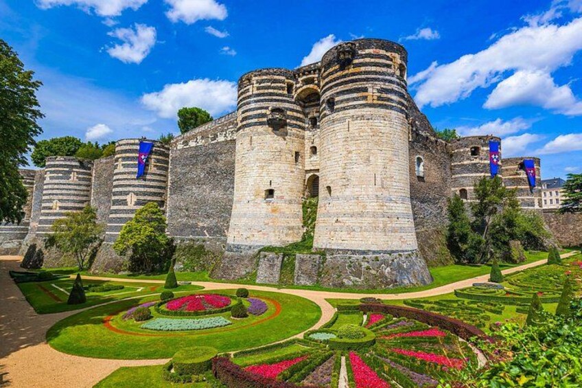 A historic castle with a moat, surrounded by well-maintained gardens and a clear blue sky. 3