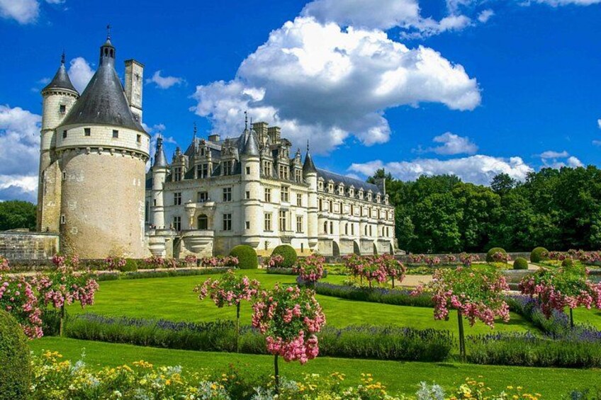 A castle with a round tower, surrounded by a well-manicured garden with various flowers and neatly trimmed hedges. 2