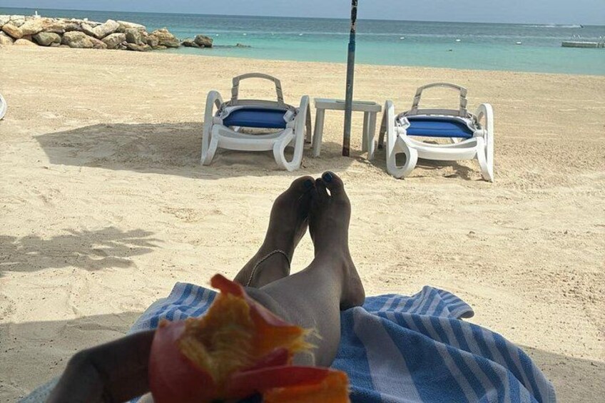 Et strandbillede med en person, der ligger på et håndklæde, fødder og to strandstole. 4