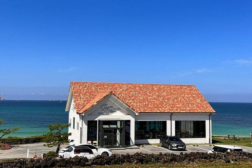 A coastal building with a red-tiled roof, a sign reading 'Team Bloom,' and parked cars in front. 1