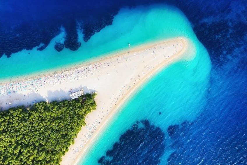 An aerial view of a beach with clear turquoise waters, a sandy shoreline, and a dense green forest area. 1
