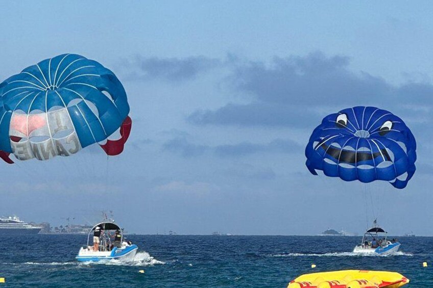 Two boats with parasails in the ocean, a distant ship, and a yellow inflatable in the foreground. 1