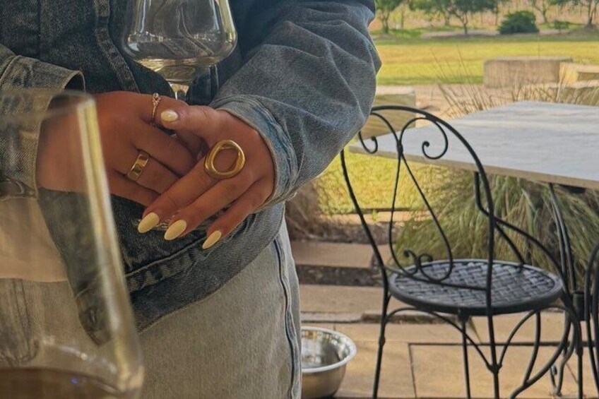 Una persona che tiene un bicchiere di vino e una bottiglia, con una sedia in metallo e un tavolo sullo sfondo. 4