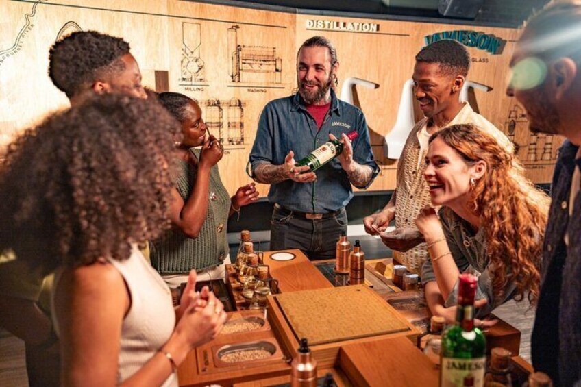 A group of people at a distillery with wooden barrels and a wooden table. 1