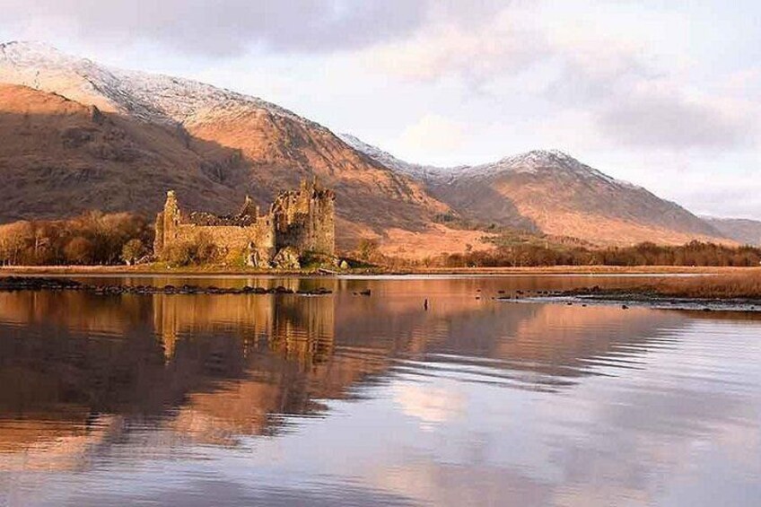 A castle by a calm lake with mountains in the background. 3
