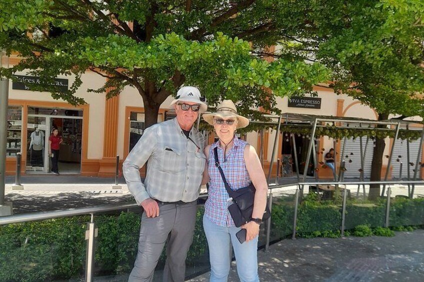 Dos personas de pie frente a un árbol, con un edificio al fondo. 3