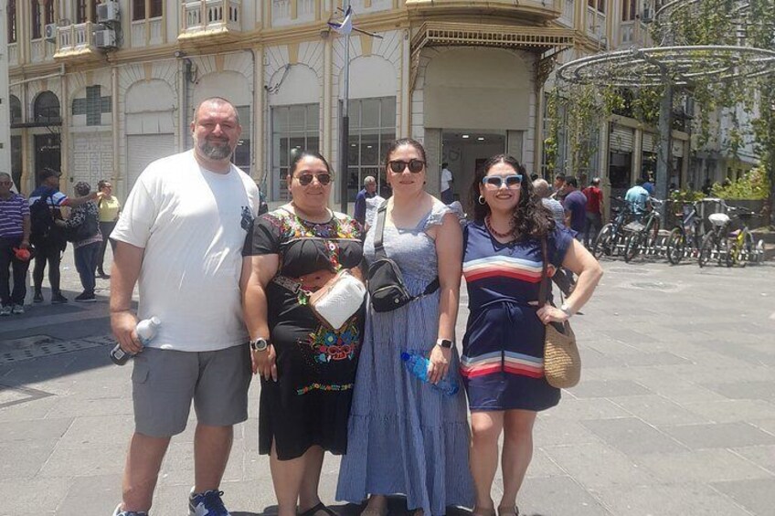 Un grupo de personas de pie en una plaza pública con edificios al fondo. 5