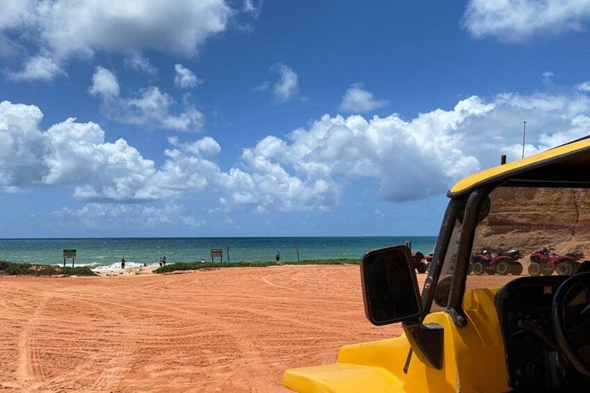 A yellow vehicle on a dirt path with a beach and ocean in the background. 3