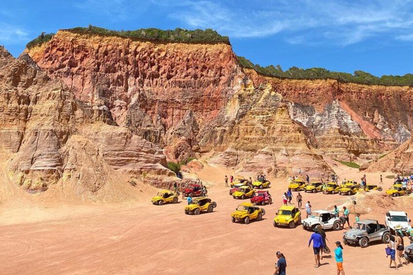 A desert landscape with red rock formations and a group of yellow and white vehicles parked on a flat area. 5