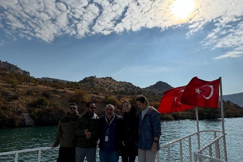 A group of people on a boat with a flag, a lake, and hills in the background. 4