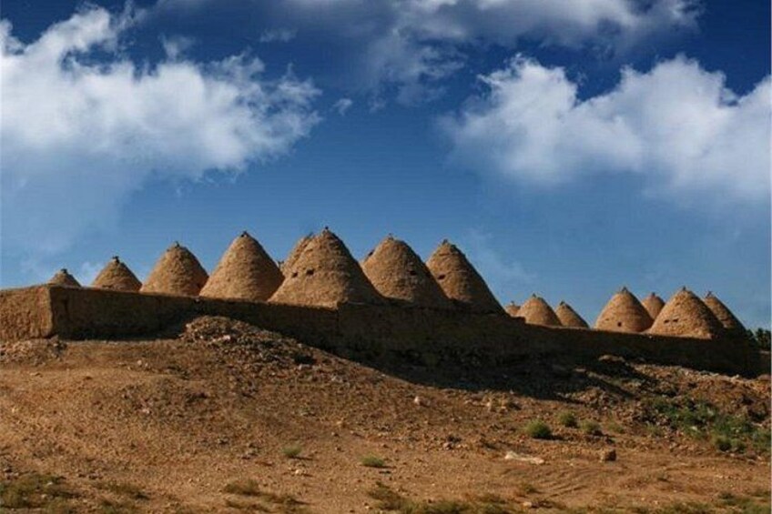 A series of conical structures on a hillside under a blue sky with clouds. 1