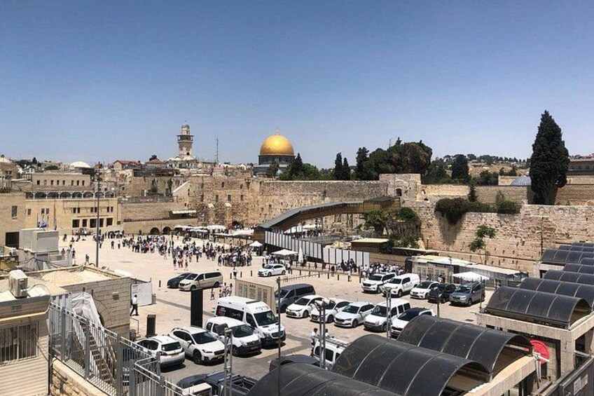 A busy parking area with vehicles, a prominent golden dome, and historic stone walls. 1