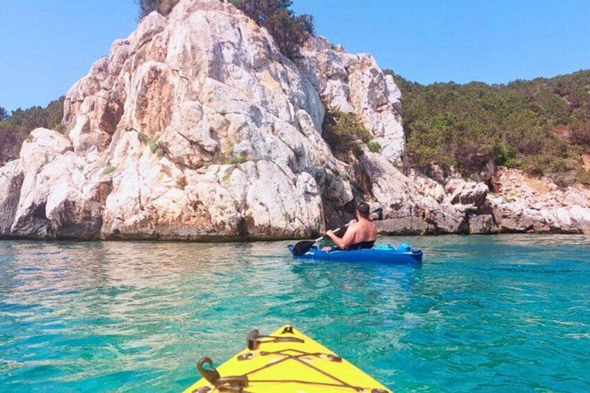 A person kayaking near a rocky coastline with clear blue water. 5