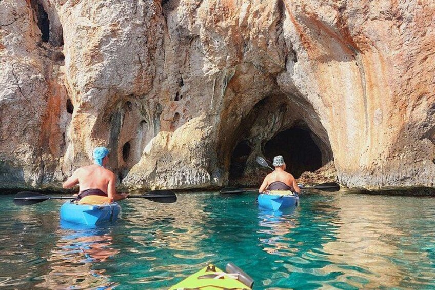 Two people kayaking through a narrow water passage between rocky cliffs. 4