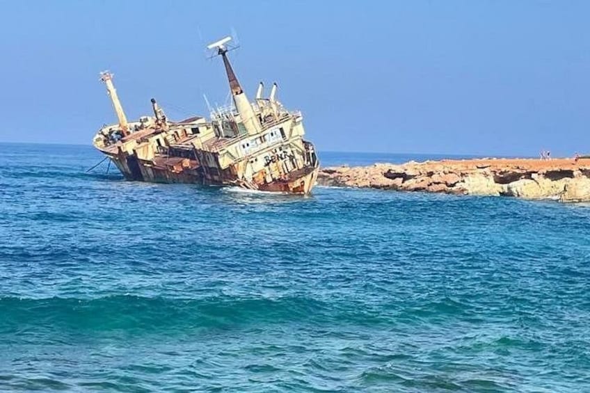 A sunken shipwreck in clear blue waters near a rocky shoreline. 1