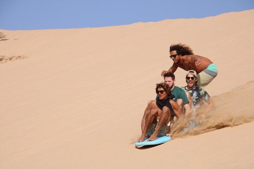 Three people sliding down a sand dune on a blue board. 5