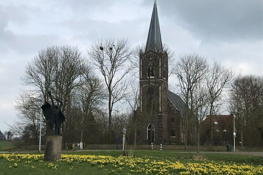 A church with a tall spire, surrounded by bare trees and a field of daffodils. 5