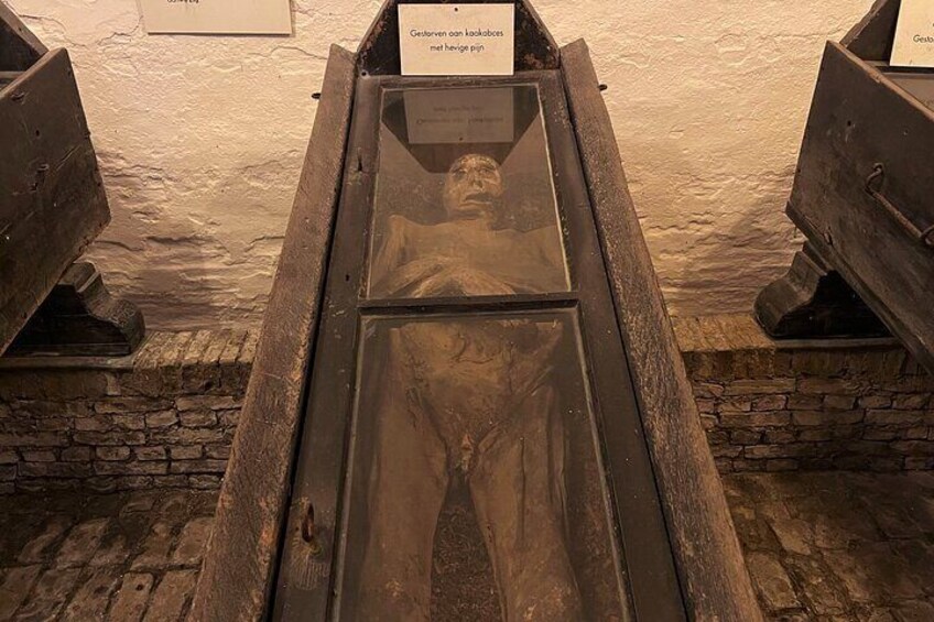 A historical display with a figure in a wooden coffin, surrounded by stone walls and a brick floor. 4