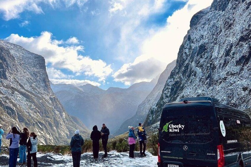 A group of people standing on a snow-covered path with a black vehicle labeled 'Cheeky Kiwi' in the foreground. 5