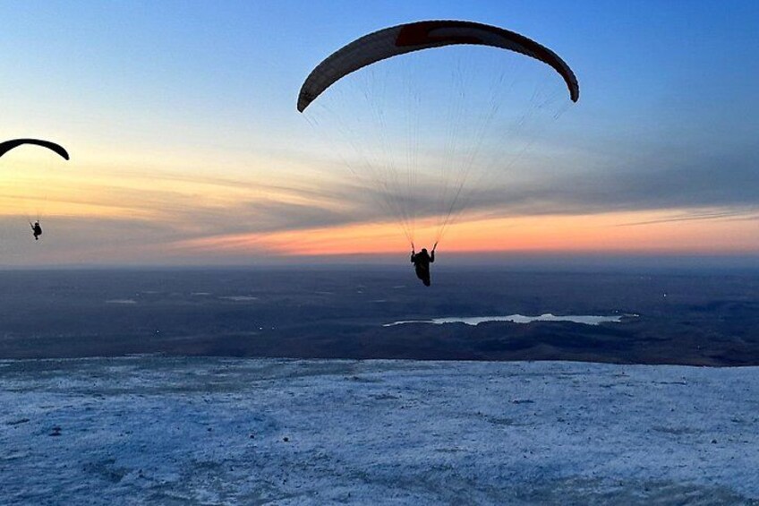 Ein Mensch gleitet mit einem Paragleiter über eine verschneite Landschaft während des Sonnenuntergangs. 2