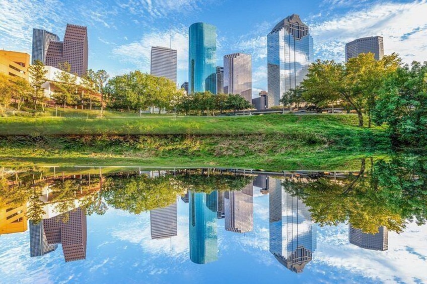 A city skyline with modern skyscrapers, a park with trees, and a calm body of water reflecting the buildings. 2