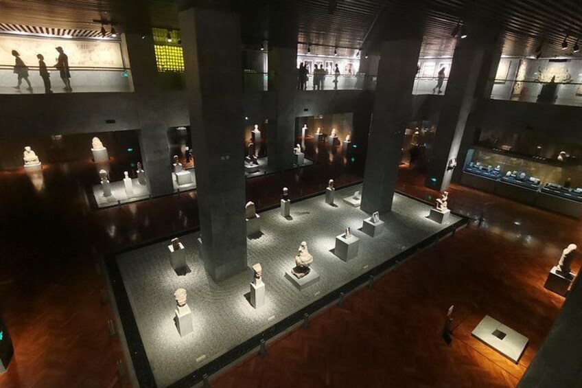 A museum interior with sculptures on display, large pillars, and visitors. 5