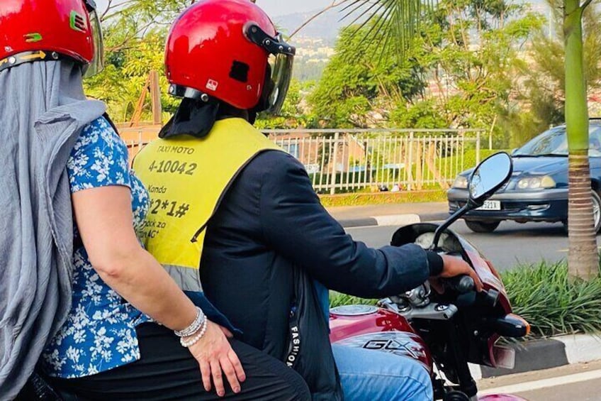 Deux personnes sont sur une moto : l’une porte un casque rouge et un gilet jaune, et l’autre porte un haut bleu à motifs floraux et une écharpe grise. 1