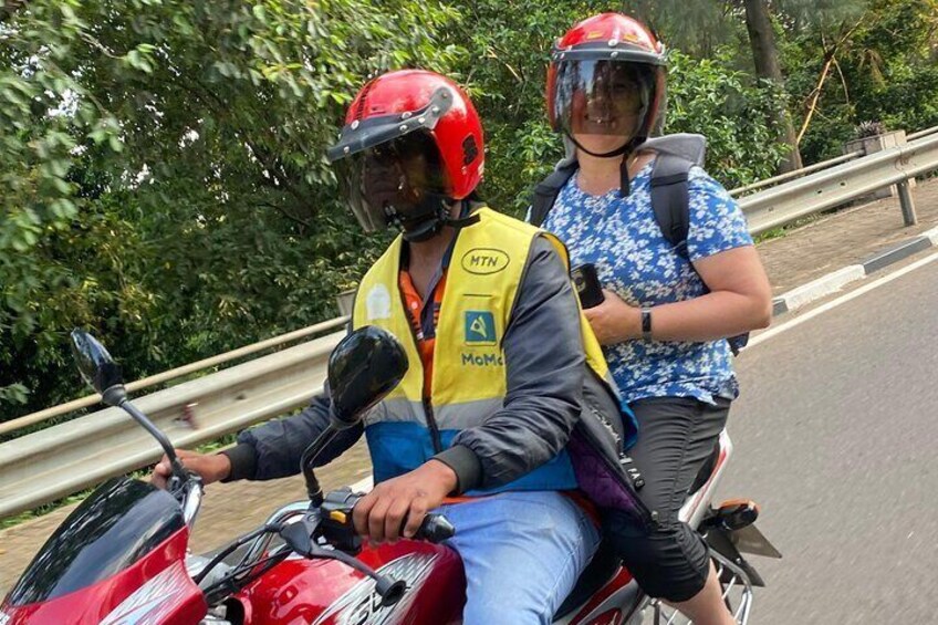 Deux personnes sont sur une moto : l’une porte un gilet jaune et l’autre un t-shirt bleu. Ils se trouvent sur une route, avec une végétation luxuriante en arrière-plan. 5