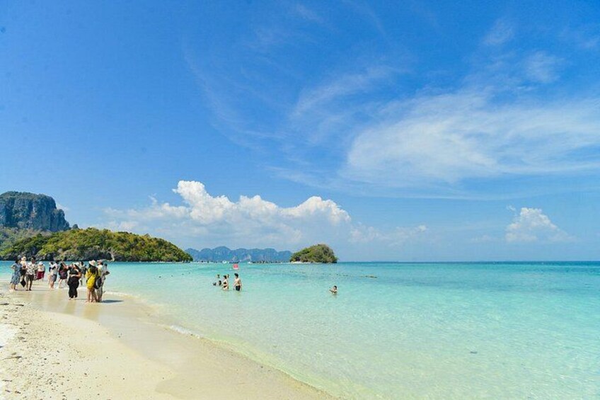 Una playa con aguas turquesas cristalinas, gente nadando y una isla a lo lejos. 3