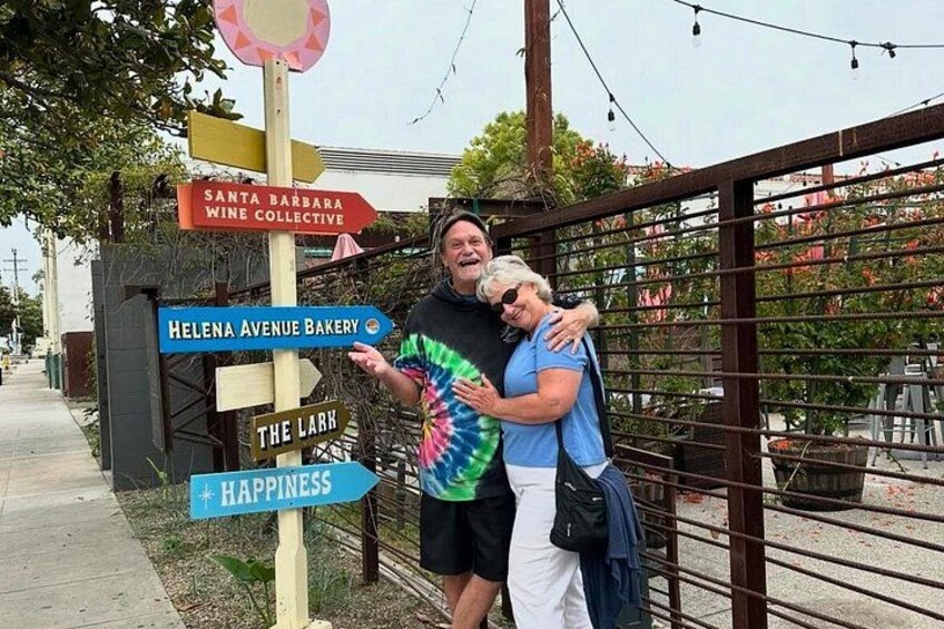 A signpost with directions to Santa Barbara Wine Collective, Helena Avenue Bakery, The Lark, and Happiness. 5