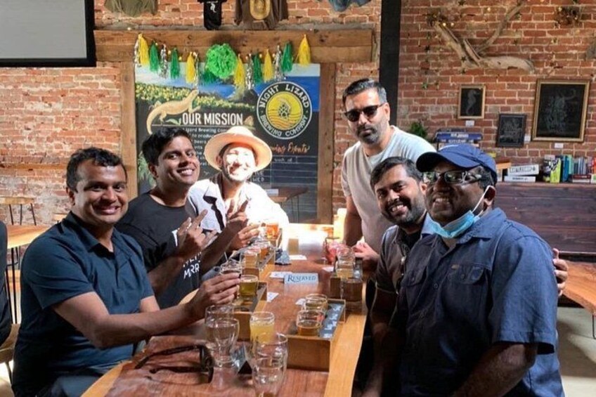 A group of people at a bar with a wooden table, glasses, and a poster on the wall. 2
