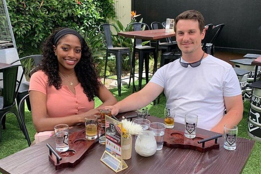 Two people sitting at an outdoor table with drinks and a menu. 3