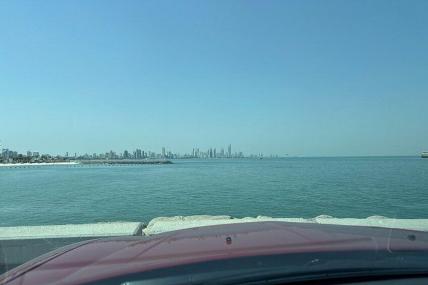 A coastal city skyline across the water, a pier, and a red vehicle in the foreground. 4