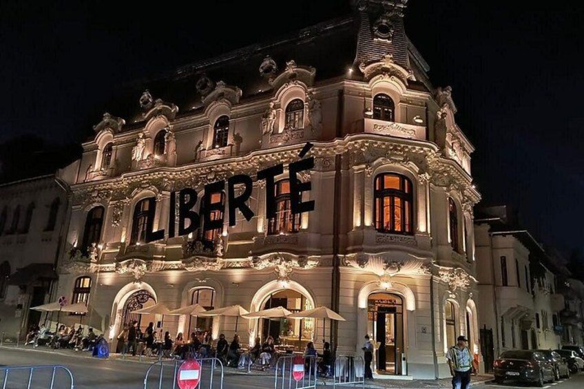 A historic building with ornate architecture and the word 'LIBERTÉ' illuminated on its facade. 4