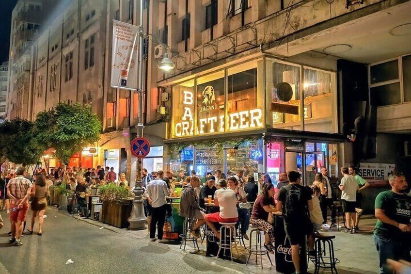 A busy street with people gathered outside a bar named 'Bar Craftier'. 5