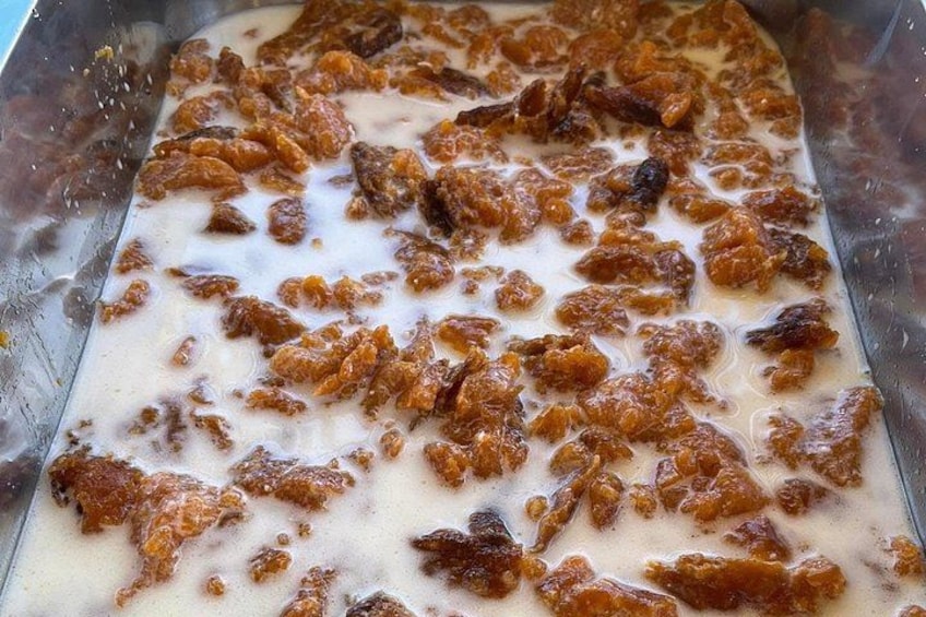 A rectangular metal tray filled with a creamy substance and brown chunks, possibly a dessert or food preparation. 2