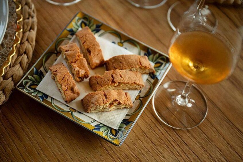 Une assiette de biscuits secs, disposés sur une assiette décorative, un verre contenant un liquide de couleur ambrée et, au fond, un panier tressé. 2