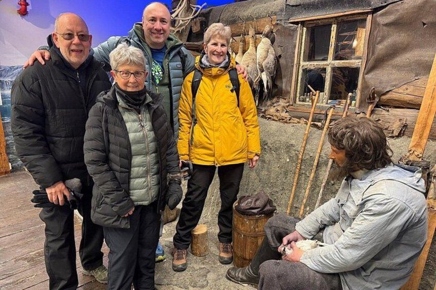Eine Gruppe von Personen steht draußen in der Nähe eines rustikalen Gebäudes mit Holzelementen und einem Fenster. 4
