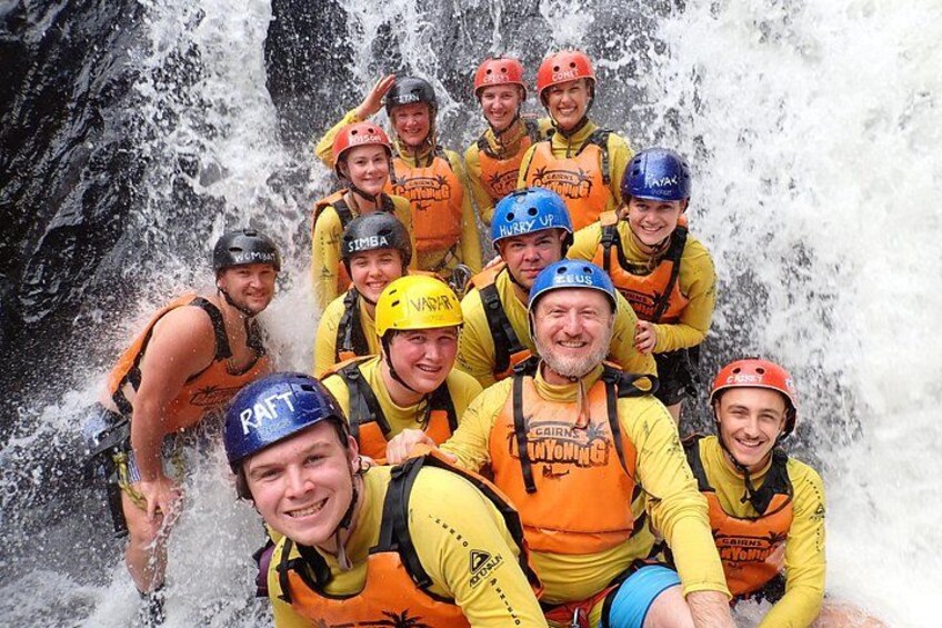 A group of people in yellow and orange life jackets and helmets, participating in a rafting activity. 1
